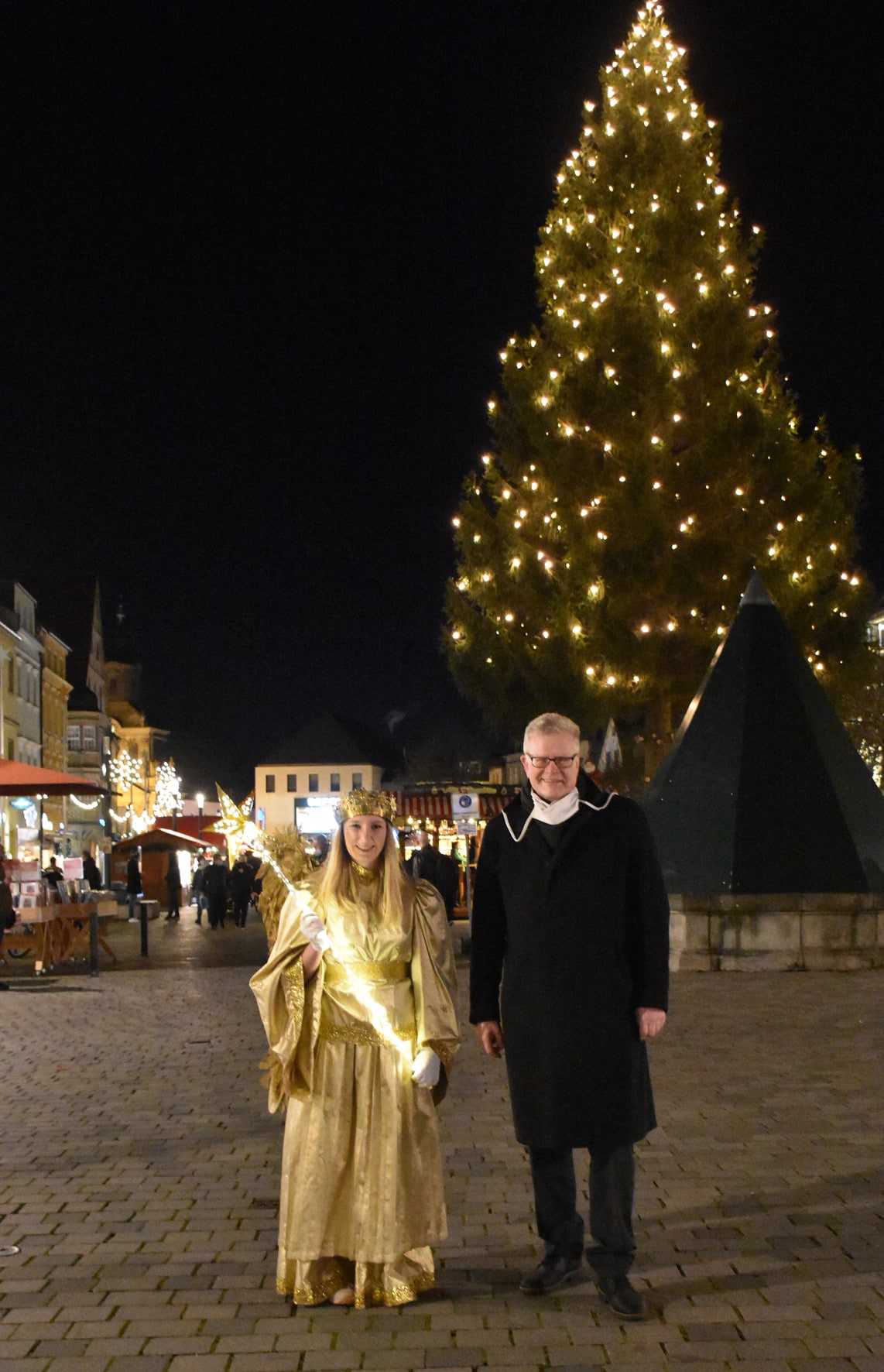 Christkind Nike Hellbach mit OB Ebersberger vor einem beleuchteten Weihnachtsbaum.n