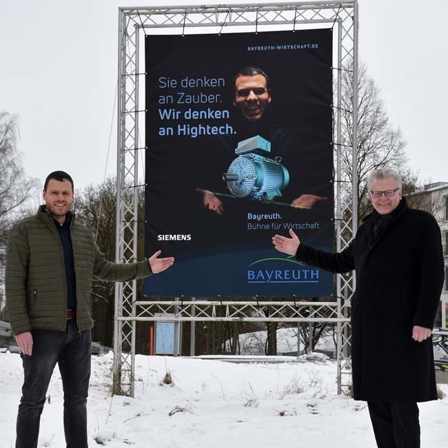Dominik Herrmann (Siemens) und Oberbürgermeister Ebersberger vor einer Plakatwand der Kampagne "Bayreuth. Bühne für Wirtschaft".