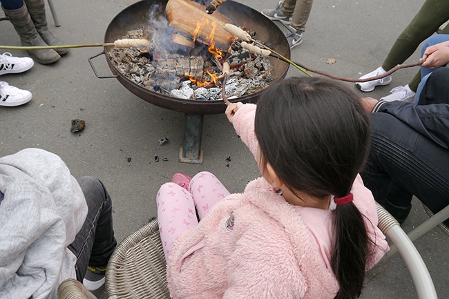 Kinder sitzen vor einer Feuerschale und backen Stockbrot